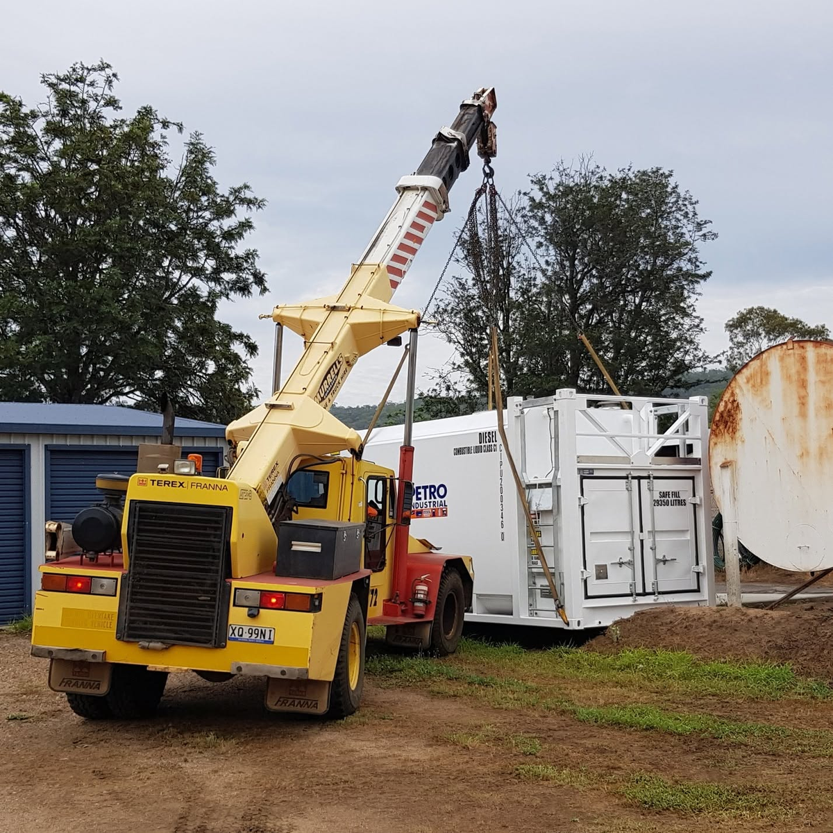 Mobile crane lifting a white PETRO fuel tank unit on site